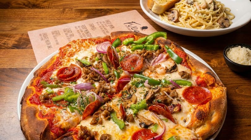 A Fuego pizza with pepperoni, sausage, peppers, onions, and mushrooms, alongside pasta and garlic bread.
