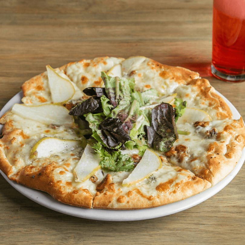 Pear and gorgonzola flatbread pizza with mixed greens, walnuts, and a red drink.