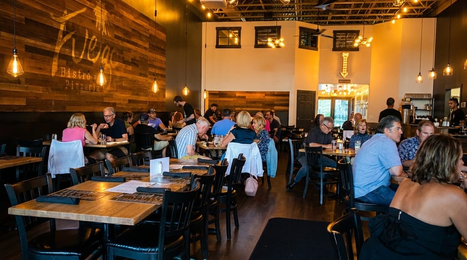 A bustling restaurant interior with patrons dining at tables and a large Fuego Bistro & Pizzeria sign.